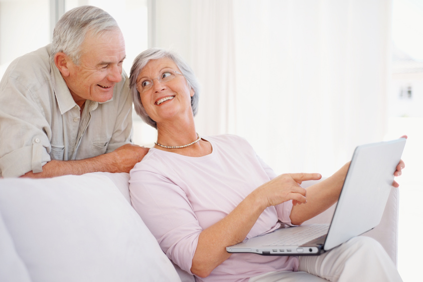Portrait of a smiling senior woman pointing at the laptop screen to her husband